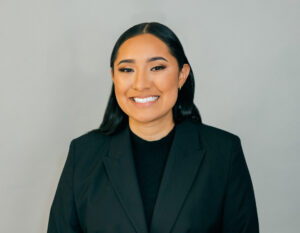 Photo of Brenda Rosas for LEAD. Brenda wears a black shirt and black jacket with slicked back hair and poses in front of a plain gray background