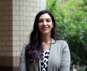 Anneeth Kaur Hundle stands in front of the Social Science Plaza and plants while wearing a gray blazer and a black and white shirt